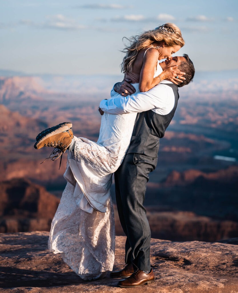 One partner holds up another partner with their feet out, nose to nose, both smiling.